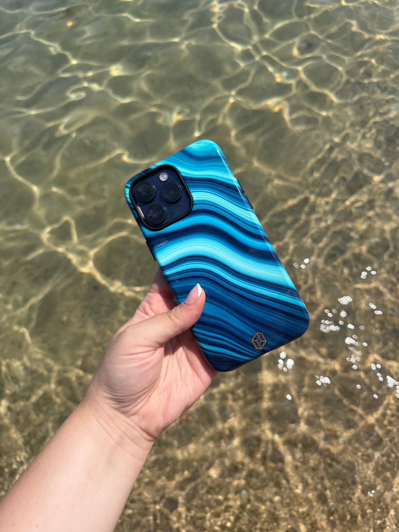 Hand holding a blue and black phone case with water in the background