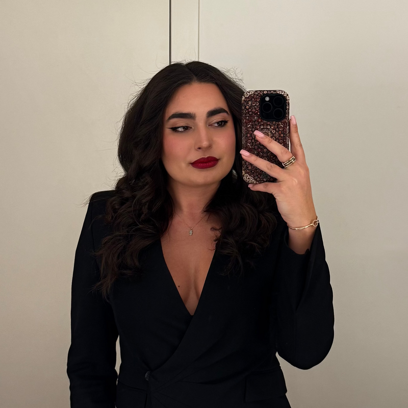 Woman taking a mirror selfie wearing a black dress against a neutral background